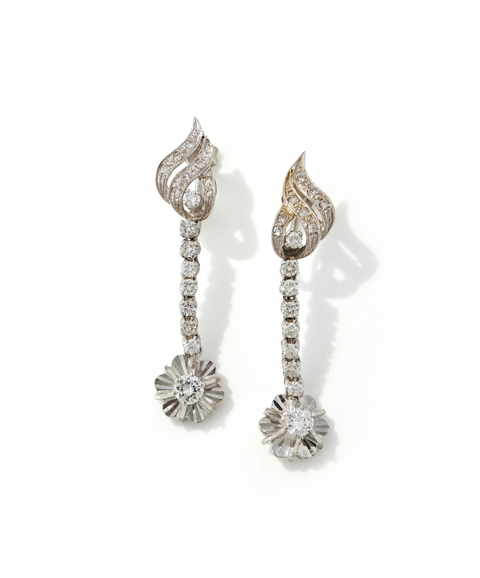 A PAIR OF DIAMOND DROP EARRINGS: A PAIR OF DIAMOND DROP EARRINGS The pierced leaf shaped pediments set with brilliant and single cut diamonds, to articulated brilliant cut diamond drops with a flowerhead shaped panel terminal with