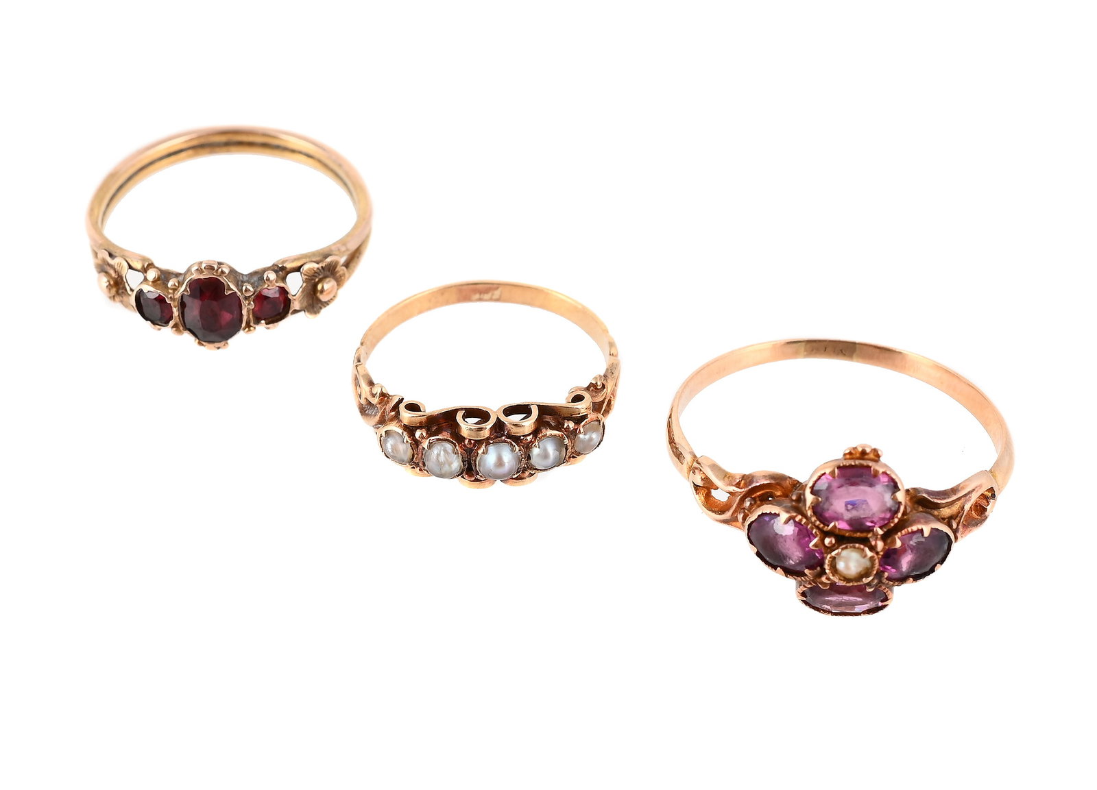 THREE VICTORIAN RINGS: THREE VICTORIAN RINGS The first with a garnet quatrefoil flower head centred with a half seed pearl, to scrolled foliate shoulders, unmarked; a three stone garnet ring with beaded and flower head