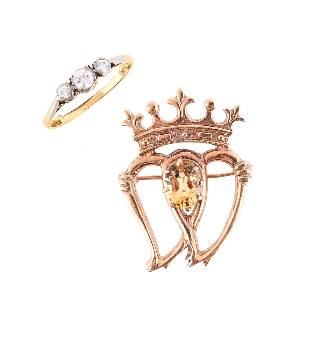 A CITRINE LUCKENBOOTH BROOCH AND A DIAMOND THREE STONE RING: A CITRINE LUCKENBOOTH BROOCH AND A DIAMOND THREE STONE RING The 9 carat gold brooch with two entwined hearts with crown surmount and oval cut citrine accent, Edinburgh 1983 hallmark;