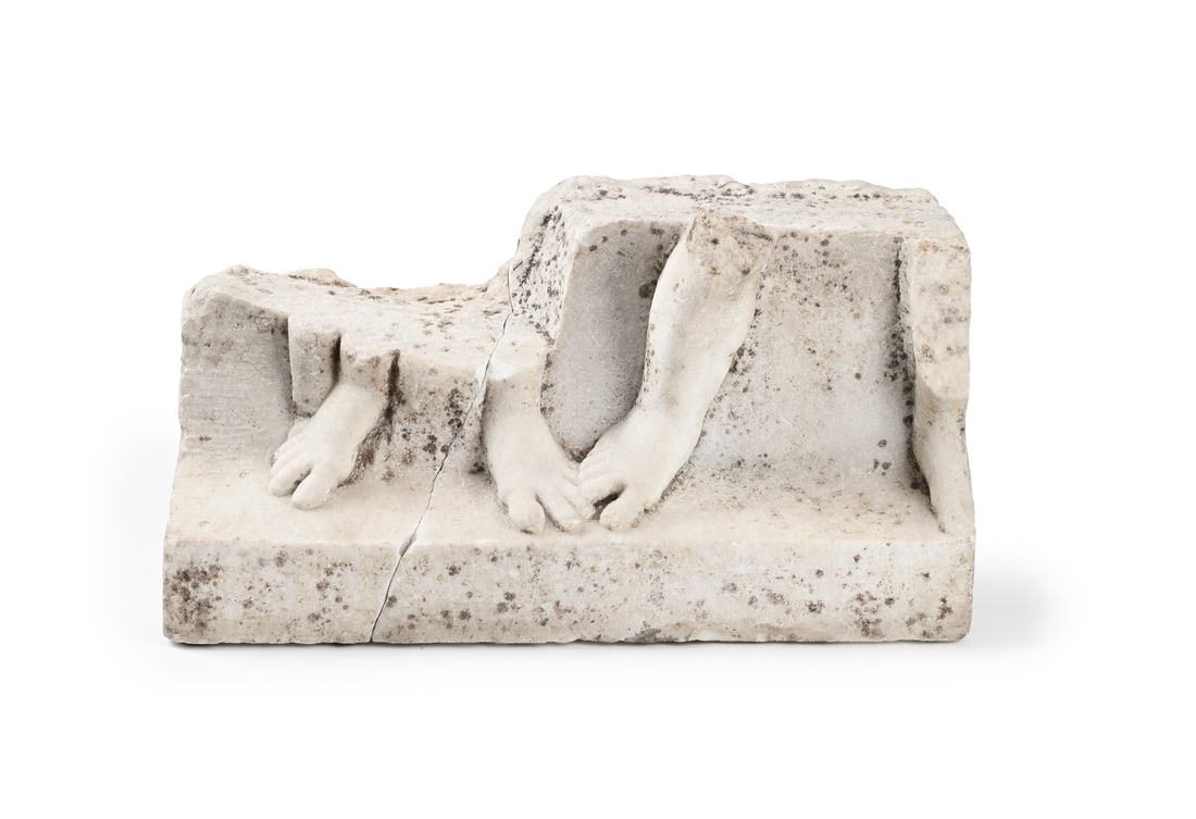 A ROMAN MARBLE RELIEF CARVED WITH PARTIALLY PRESERVED LOWER LEGS AND FEET, CIRCA 2ND CENTURY: A ROMAN MARBLE RELIEF CARVED WITH PARTIALLY PRESERVED YOUTHFUL LOWER LEGS AND FEET CIRCA 2ND CENTURY A.D. A fragment from a larger sculpture 24cm high, 44cm wide ProvenanceAcquired Amy Perlin, Antique