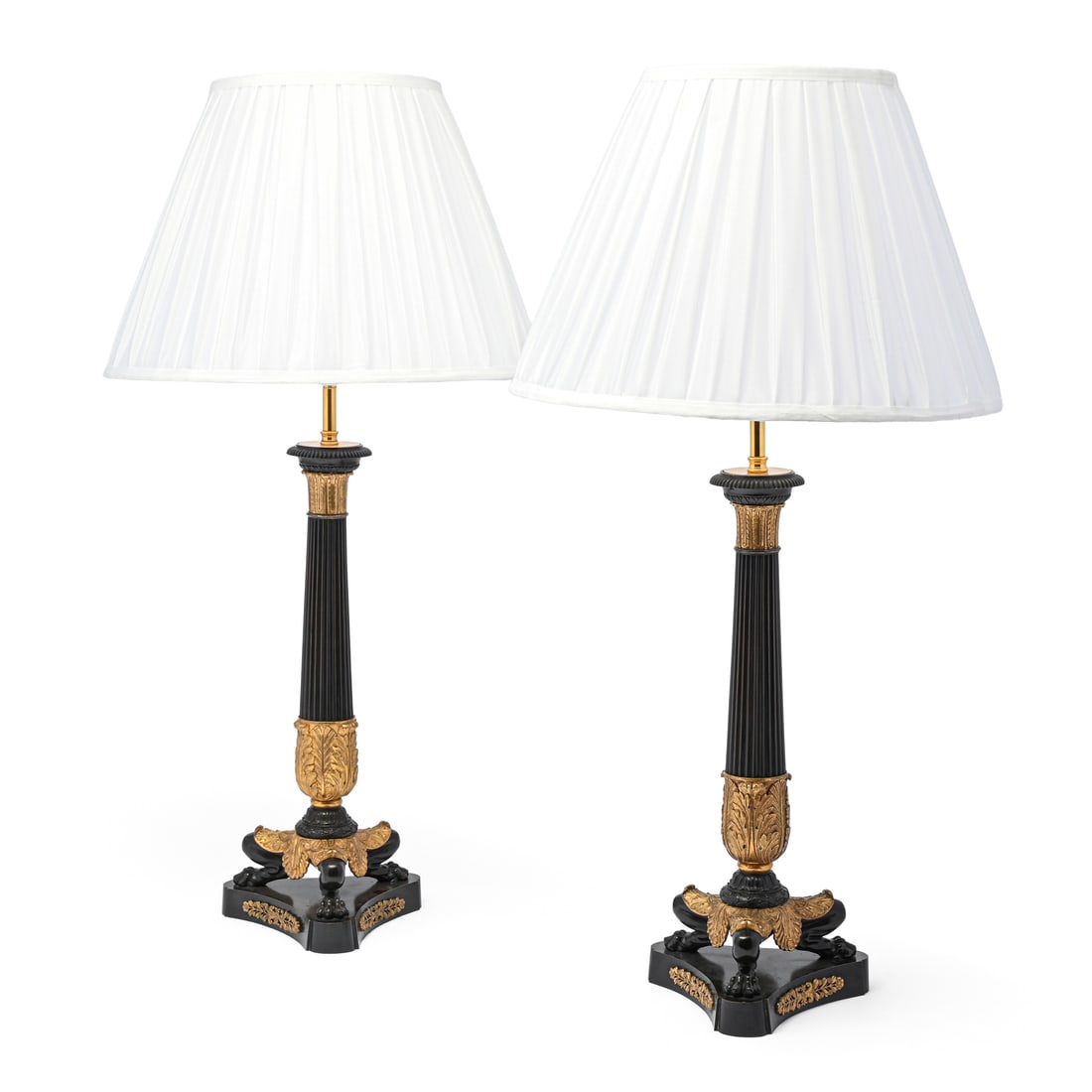 A PAIR OF GILT AND PATINATED BRONZE CANDLESTICK TABLE LIGHTS, FRENCH, 19TH CENTURY: A PAIR OF GILT AND PATINATED BRONZE CANDLESTICK TABLE LIGHTS FRENCH, 19TH CENTURY With Herculaneum style triform bases, later part fitted for electricity44.5cm high, 77cm high including the shades