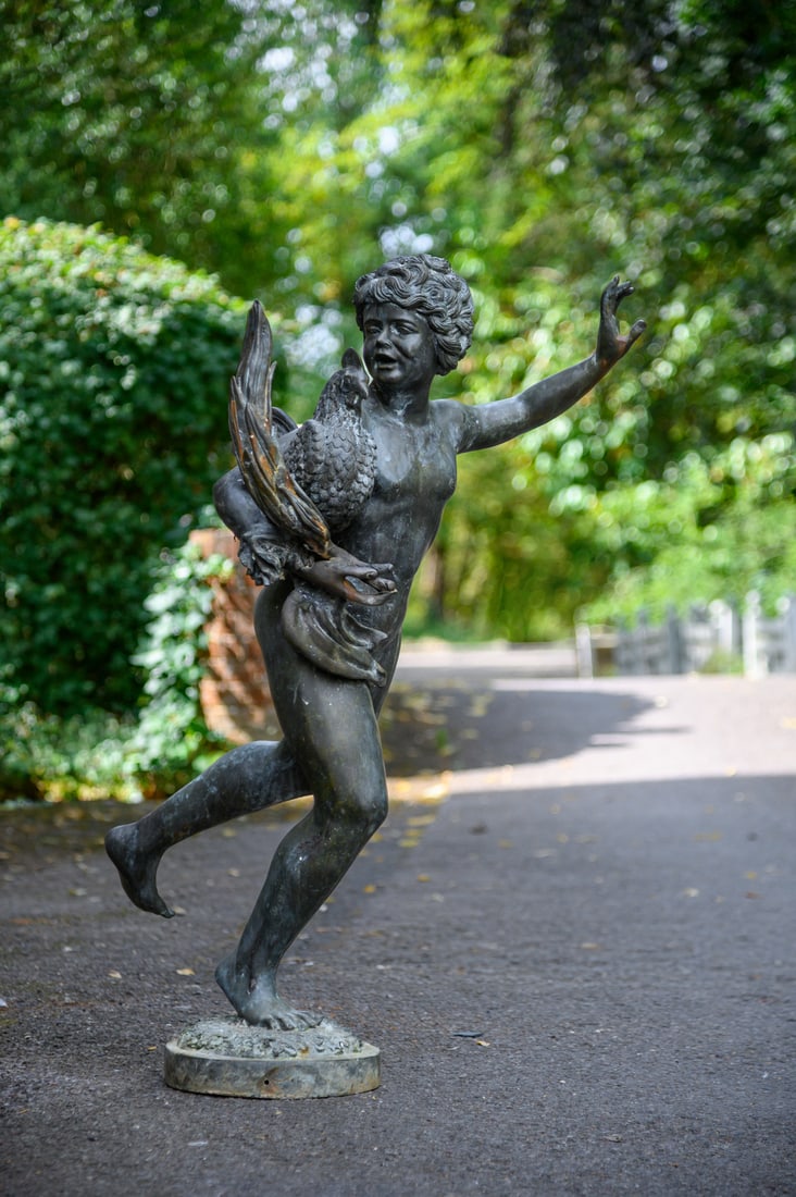 A BRONZED GARDEN SCULPTURE OF A YOUNG BOY HOLDING A COCKEREL, IN THE POMPEIAN MANNER, 20TH CENTURY: A BRONZED GARDEN SCULPTURE OF A YOUNG BOY HOLDING A COCKEREL IN THE POMPEIAN MANNER, 20TH CENTURY107cm high, the base 28cm diameter