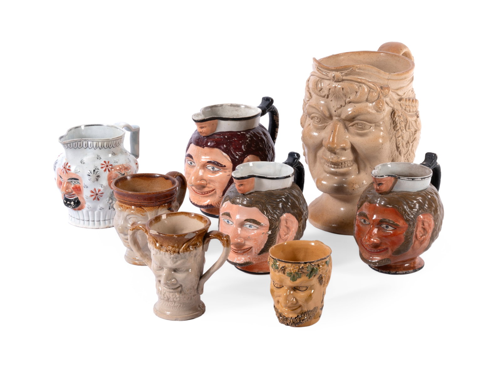AN ENGLISH SALT GLAZED STONEWARE SATYR-MASK HARVEST JUG, 19TH CENTURY, AND SEVEN FURTHER MASK JUGS: AN ENGLISH SALT GLAZED STONEWARE SATYR-MASK HARVEST JUG MID 19TH CENTURY 24cm high Together with seven other English pottery and stoneware mask jugs, 15cm high and smaller (8) Condition Report: The