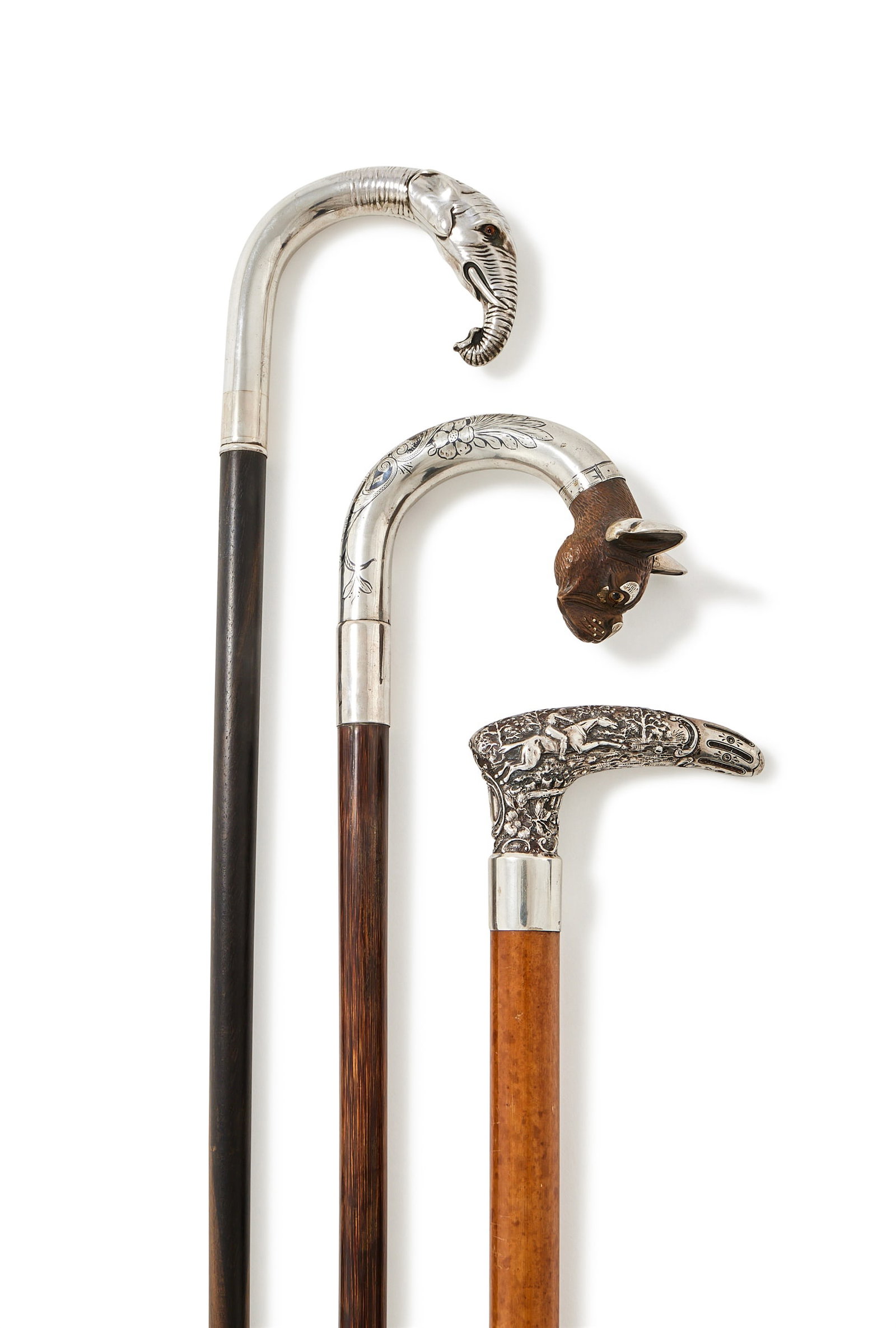 THREE CONTINENTAL FIGURAL WALKING STICKS: A SILVER MOUNTED ELEPHANT WALKING STICKSTAMPED 925The Macassa ebony cane with a silver elephant handle, with glass eyes89.5cm longTogether with:A SILVER MOUNTED, NIELLO AND CARVED WALNUT DOG WALKING S