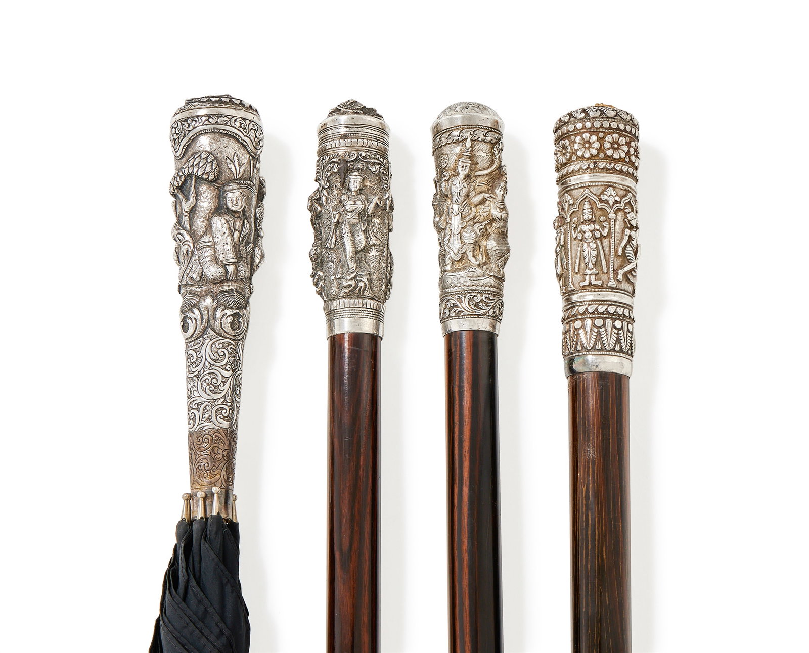 Y THREE SOUTH ASIAN WALKING STICKS AND A PARASOL: Y A SOUTH ASIAN SILVER HANDLED WALKING STICKUNMARKEDThe rosewood cane with a silver pommel, chased with figures and foliage to a foliate ground, the top with a foo dog mask91cm longTogether with:A SOU