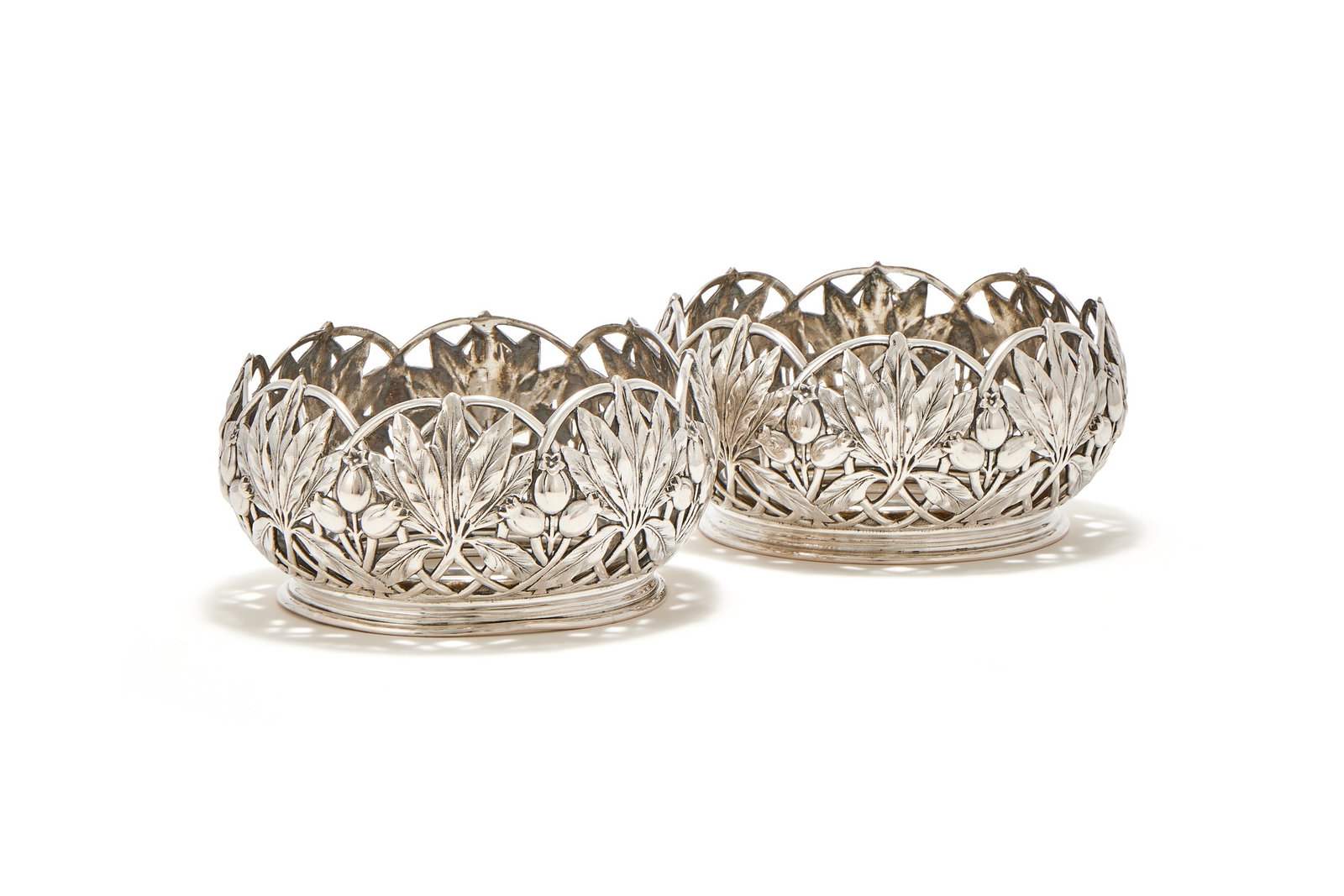 A PAIR OF GERMAN SILVER BOTTLE HOLDERS, M. H. WILKENS & SÖHNE, BREMEN-HEMELINGEN: A PAIR OF GERMAN SILVER BOTTLE HOLDERSM. H. WILKENS & SÖHNE, BREMEN-HEMELINGEN, POST 1886 .800 STANDARDThe wirework bodies chased with foliage and on circular bases13.5cm diameter447g (14.4 oz)