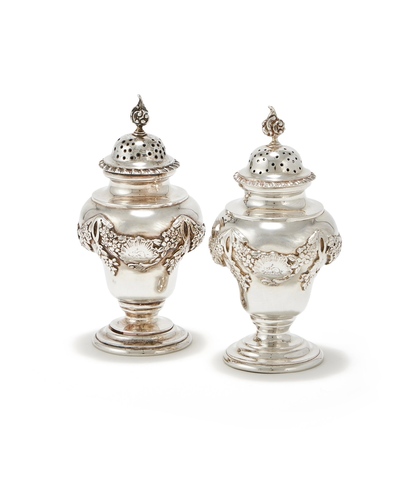 A PAIR OF EDWARDIAN SILVER PEPPERETTES, CHARLES STUART HARRIS, LONDON 1902: A PAIR OF EDWARDIAN SILVER PEPPERETTESCHARLES STUART HARRIS, LONDON 1902With chased C-scroll finial to the domed and gadrooned covers, the bodies with floral swags, engraved with crests and on circula