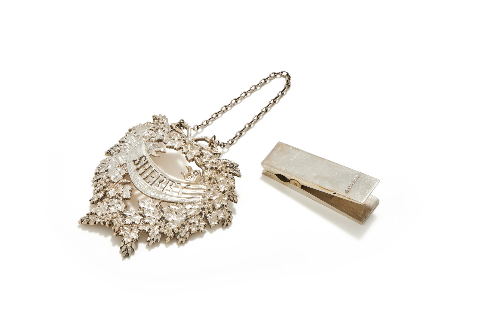 ASPREY & CO. LTD., A SILVER DECANTER LABEL AND A PAPER CLIP, LONDON 1964: ASPREY & CO. LTD.A SILVER DECANTER LABEL, LONDON 1964Chased with grape vines and pierced Sherry8.5cm longTogether with:ASPREY & CO. LTD.A SILVER PAPER CLIP, LONDON 20016cm long138g (4.45 oz) gross