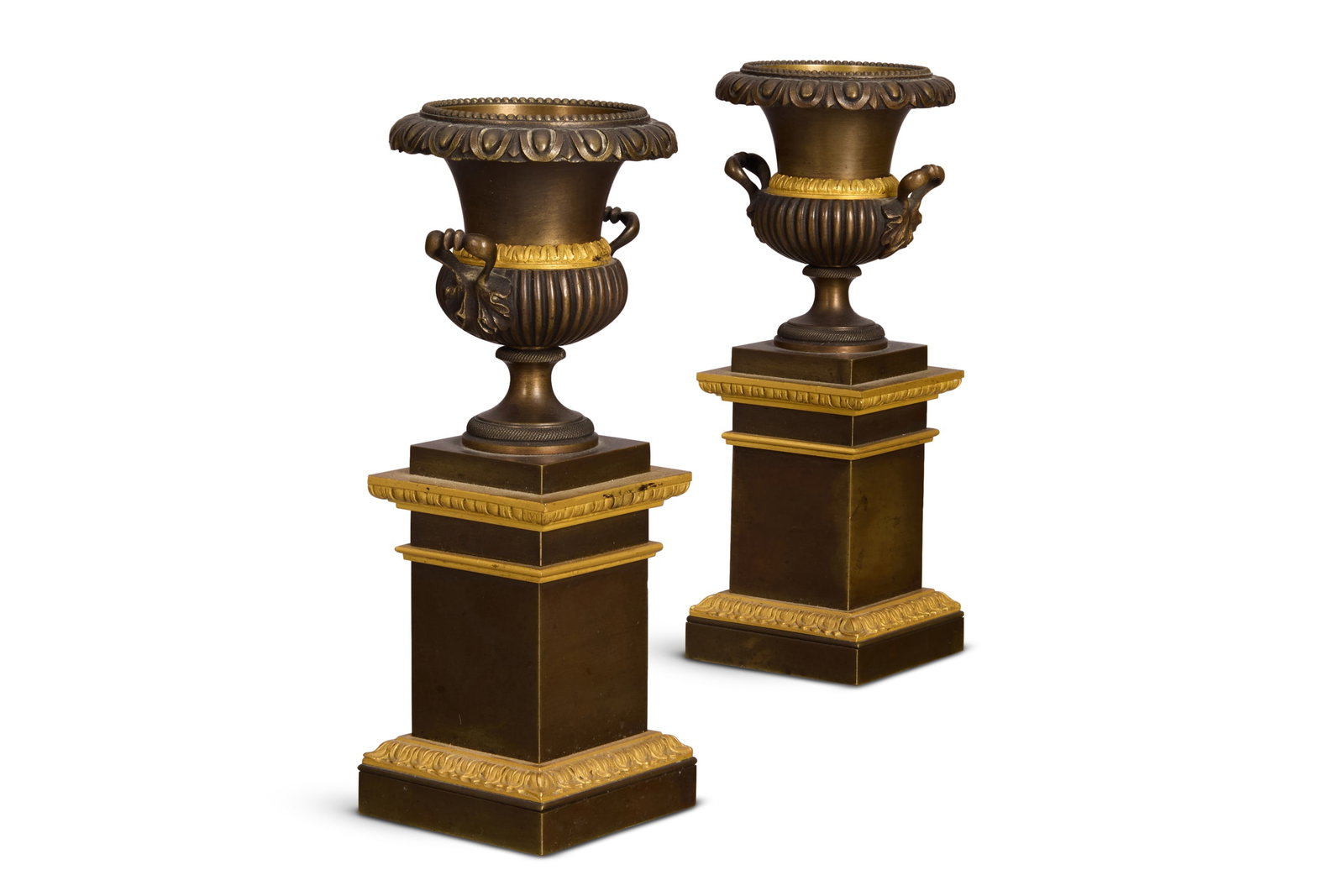 A VERY SMALL PAIR OF EMPIRE GILT AND PATINATED BRONZE URNS, EARLY 19TH CENTURY: A VERY SMALL PAIR OF EMPIRE GILT AND PATINATED BRONZE URNS EARLY 19TH CENTURY In the Classical manner, twin handled, gadrooned bellied form, stepped plinths 14cm high
