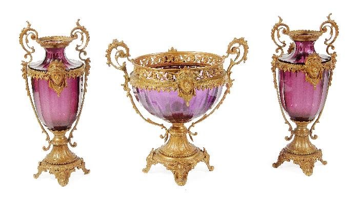 A garniture of three Continental cut amethyst glas: A garniture of three Continental cut amethyst glass and gilt bronze mounted twin handled vases, late 19th century, comprising one with openwork foliate cast gallery with centered masks above the bowl,