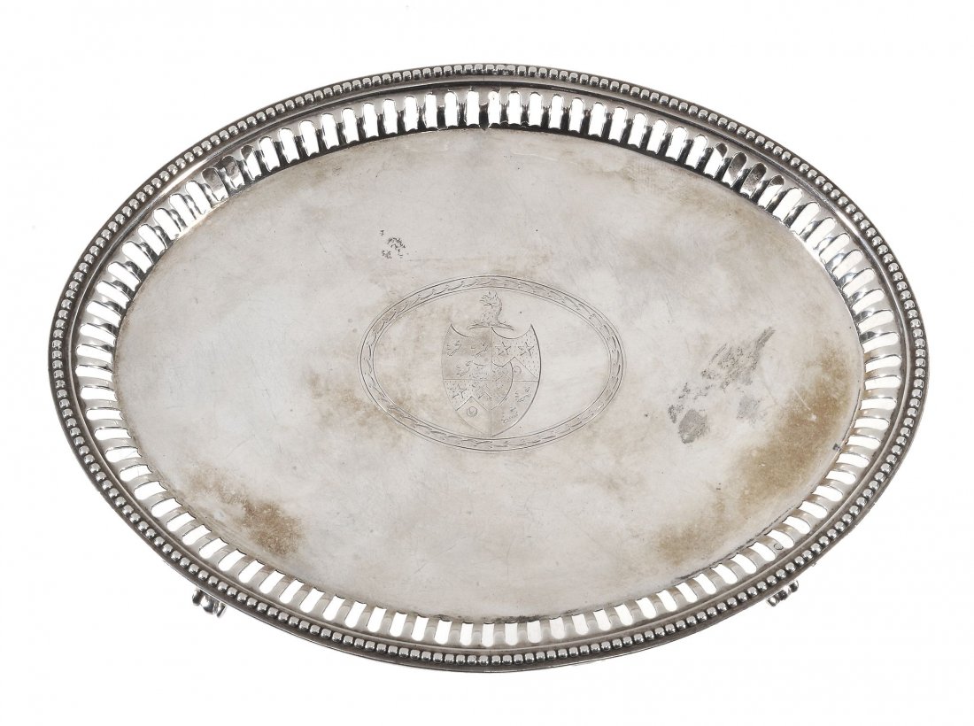 A George III oval silver tea pot stand by Elizabeth: A George III oval silver tea pot stand by Elizabeth Jones , London 1785, with a pierced and beaded border, engraved with an armorial within laurel leaf cartouche, on four bracket feet, 18cm (7in) long