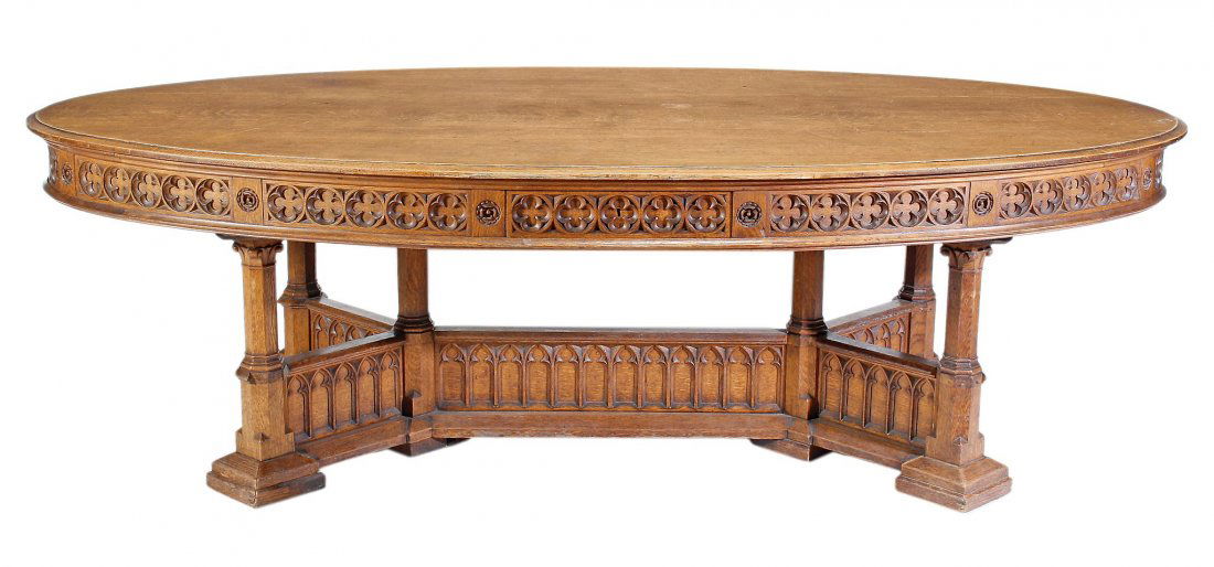 A Victorian Gothic Revival oak library table, circa: A Victorian Gothic Revival oak library table, circa 1860, the oval top with moulded edge, above a repeated quatrafoil carved frieze incorporating four drawers, above six octagonal columnar supports an