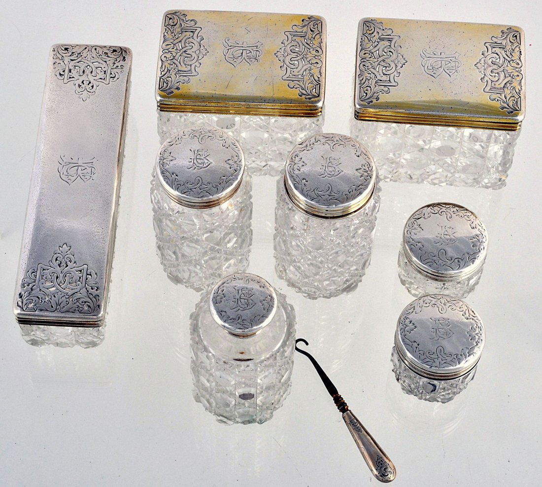Seven cut glass dressing table pots and jars with: Seven cut glass dressing table pots and jars with silver covers by Thomas Johnson I, London 1857, with engraved foliate decoration and initials, the largest 18cm long, the smallest 4.7cm diameter; and