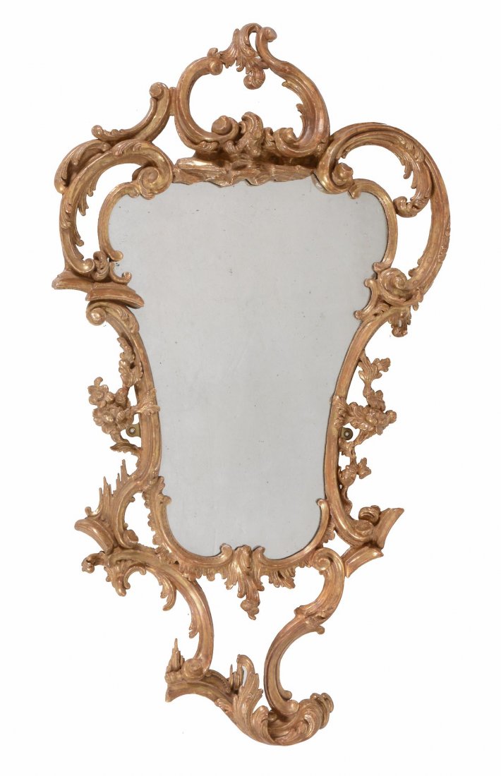 A George III carved giltwood wall mirror, circa 1760: A George III carved giltwood wall mirror, circa 1760, in the manner of Thomas Johnson, the shaped plate within the cartouche shaped frame carved throughout with C scroll motifs, acanthus and sprigs of