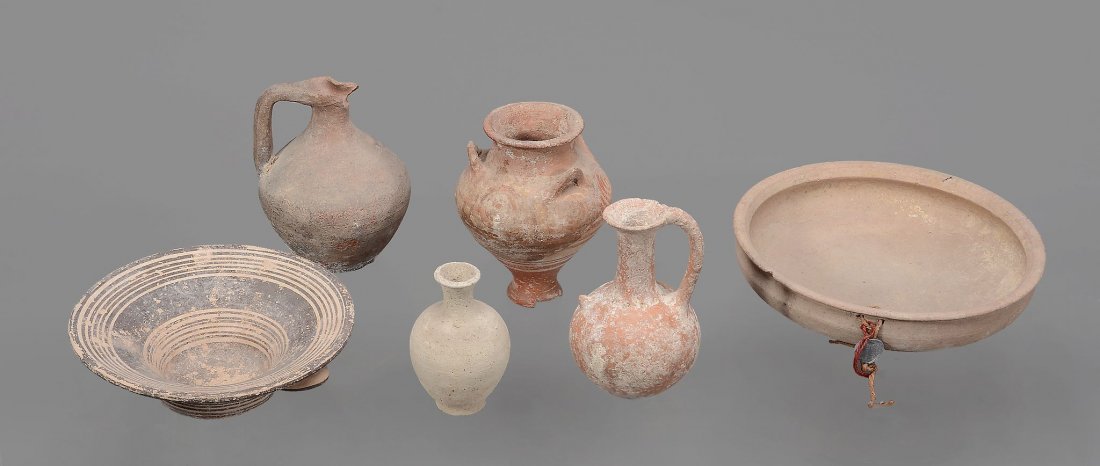 A group of pottery vessels , including a buff coloured: A group of pottery vessels , including a buff coloured bowl, a piriform storage vessel with three handles and added decoration, a dark brown coloured bowl with broad outward turned rim and decoration 