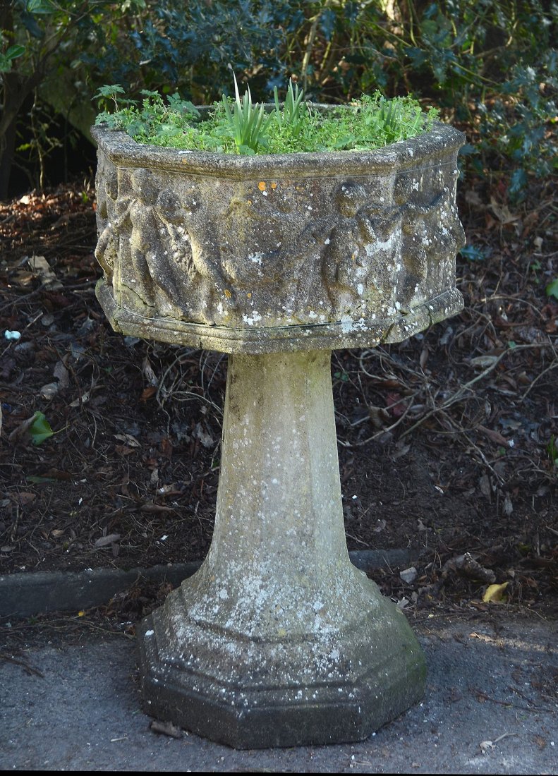 A stone composition garden planter, 20th century, of: A stone composition garden planter, 20th century, of octagonal section, the basin with cavorting amorini cast in relief to the sides, on a spreading octagonal section pedestal and base, 106cm high, 62