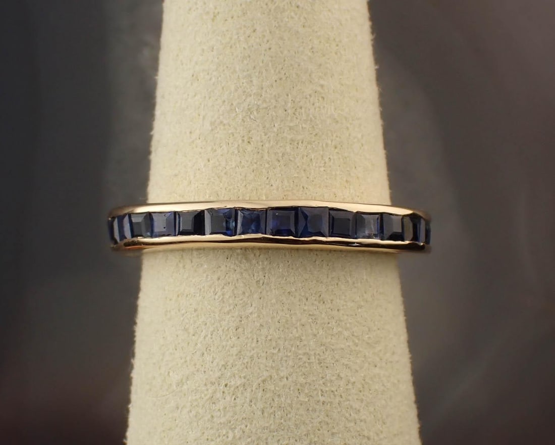 SAPPHIRE AND FOURTEEN KARAT GOLD ETERNITY BAND: SAPPHIRE AND FOURTEEN KARAT GOLD ETERNITY BAND, yellow gold channel set with 32 square-cut sapphires together weighing 2.35 cttw. The ring weighs 3.1 grams and is stamped "14K" and "2.35cts". Ring siz