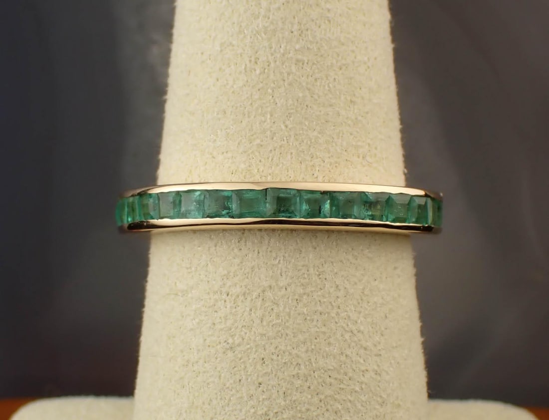 EMERALD AND FOURTEEN KARAT GOLD ETERNITY BAND: EMERALD AND FOURTEEN KARAT GOLD ETERNITY BAND. The yellow gold band is channel set with 33 square-cut emeralds together weighing 1.80 cttw. The band weighs 3.4 grams and is stamped "14K" and "1.80cts"