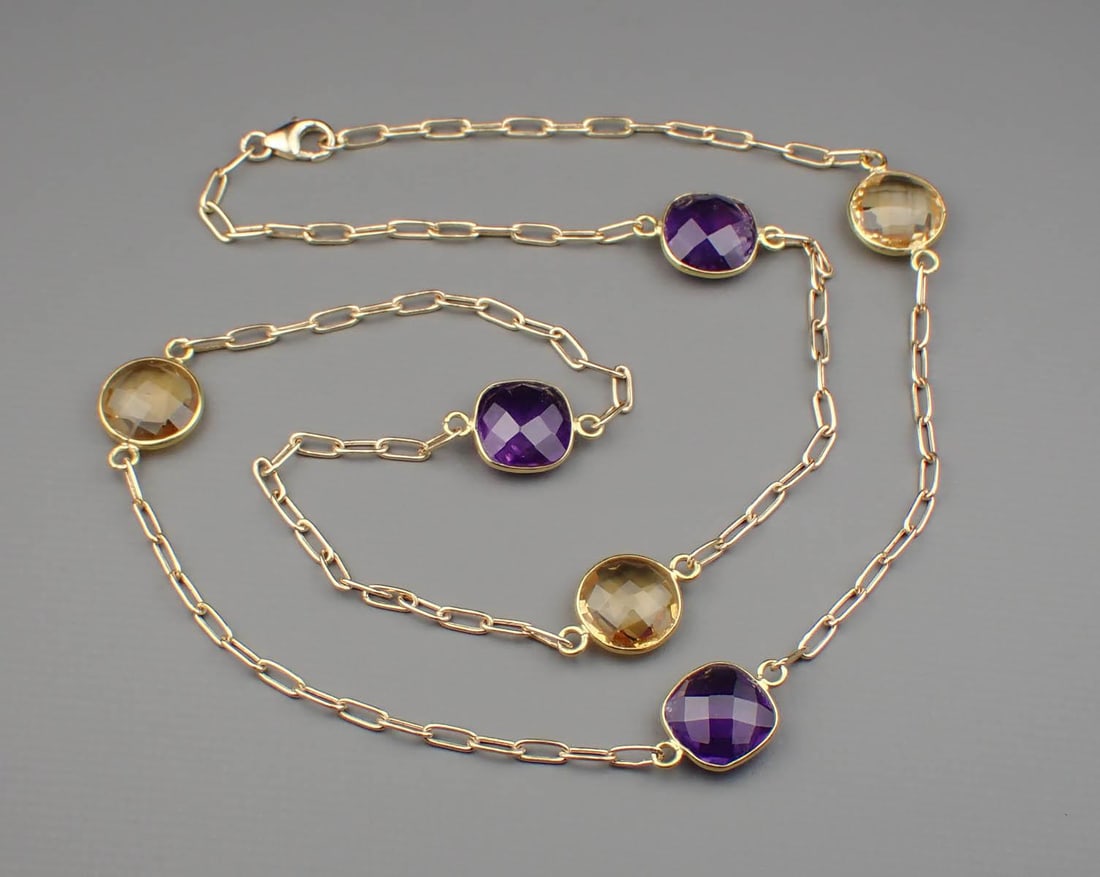 AN AMETHYST AND CITRINE STATION CHAIN: AN AMETHYST AND CITRINE STATION CHAIN: 14k yellow gold paperclip chain with a lobster claw clasp, featuring four cushion double checkerboard-cut amethysts weighing approximately 8.00 cttw, and three