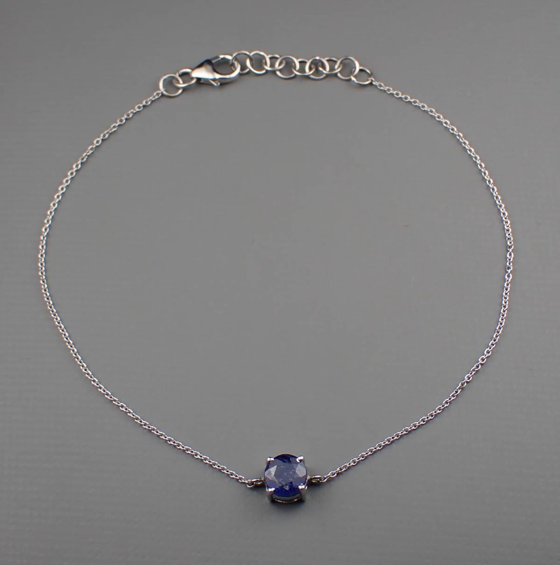 SAPPHIRE & 14K GOLD SOLITAIRE BRACELET: SAPPHIRE & 14K GOLD SOLITAIRE BRACELET:adjustable length white gold cable chain bracelet ending with a lobster claw clasp and featuring a four-prong pendant set with a round-cut blue sapphire weighing