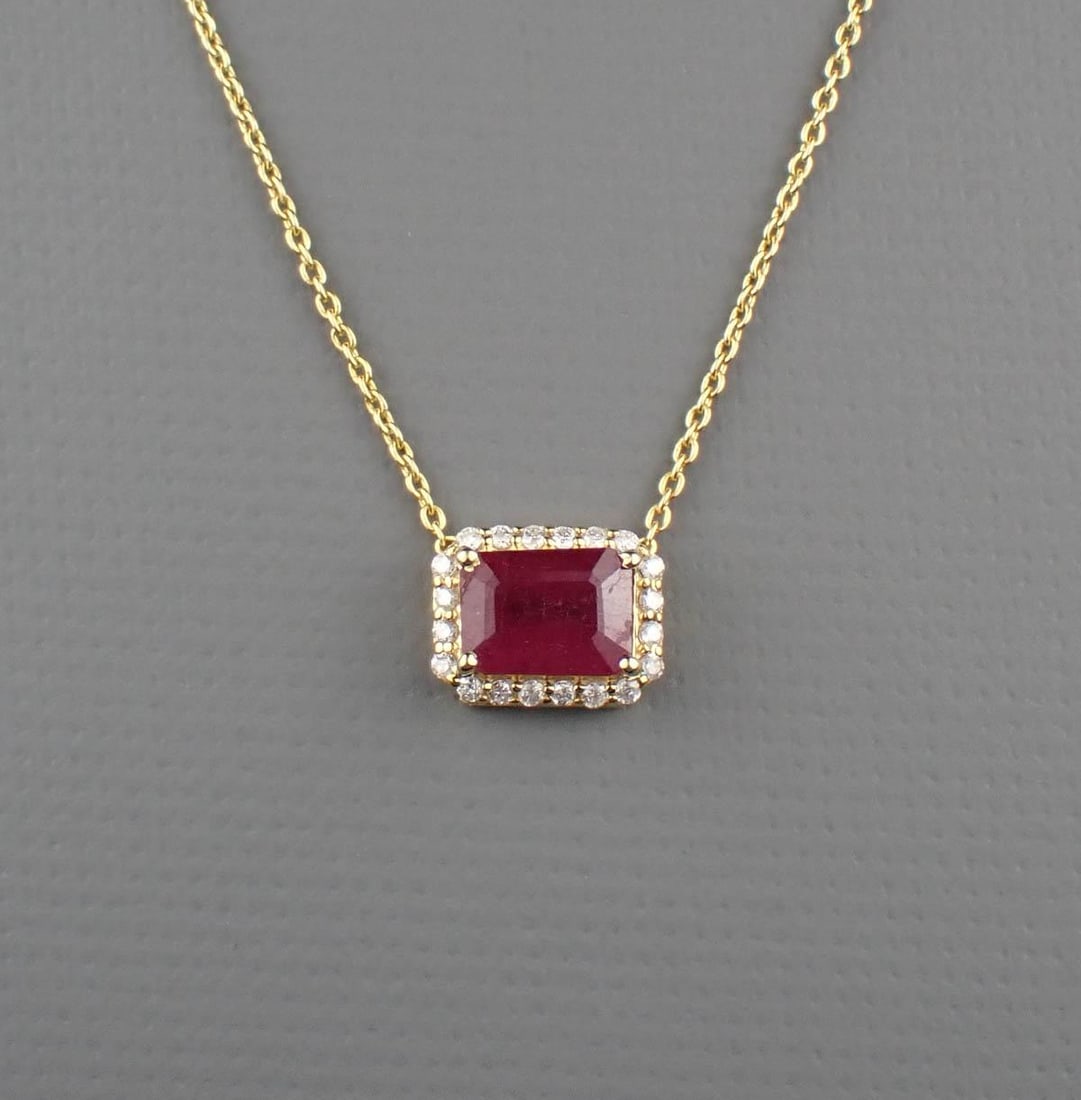 RUBY, DIAMOND HALO & 14K GOLD NECKLACE: adjustable length yellow gold cable chain featuring a yellow gold pendant with 20 round-cut diamonds set round an emerald-cut ruby weighing approximately 1.29 cts. The necklace weighs 2.2 grams, is st