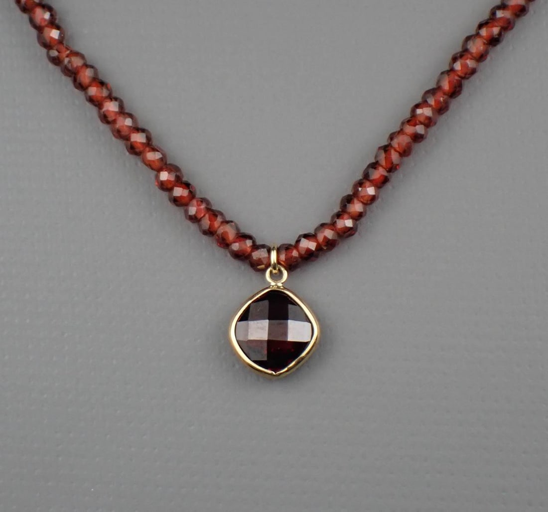 GARNET & 14K GOLD NECKLACE: GARNET & 14K GOLD NECKLACE:adjustable length necklace strung with garnet rondelle beads ending with a length of yellow gold and spring ring clasp and featuring a yellow gold pendant bezel set with a c