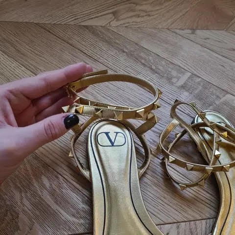 VALENTINO GARAVANI ROCKSTUD SANDALS: Metallic Gold Leather Ankle Strap HeelsAn iconic pair of Valentino Garavani Rockstud sandals crafted in luxurious metallic gold leather with the House’s signature pyramid stud detailing.Elegant yet