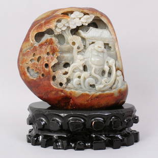 1123: A VERY FINE CHINESE CARVED HETIAN JADE BOULDER: FINELY CARVED BOULDER WITH SKIN OF RUSSET. CARVED TO DEPICT FIGURE WATERING THE PLANTS UNDER THE TREES IN FRONT OF BOUDINGS, COMES WITH CARVED WOODEN STAND.