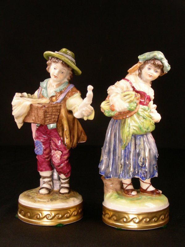 ANTIQUE VOLKSTEDT PORCELAIN FIGURES BOY GIRL: Both beautifully hand painted. Dressed in peasant style tattered clothes. Girl holds a basket of vegetables and boy is holding a figurine pulled from a basket. Both stand on round bases trimmed hand p
