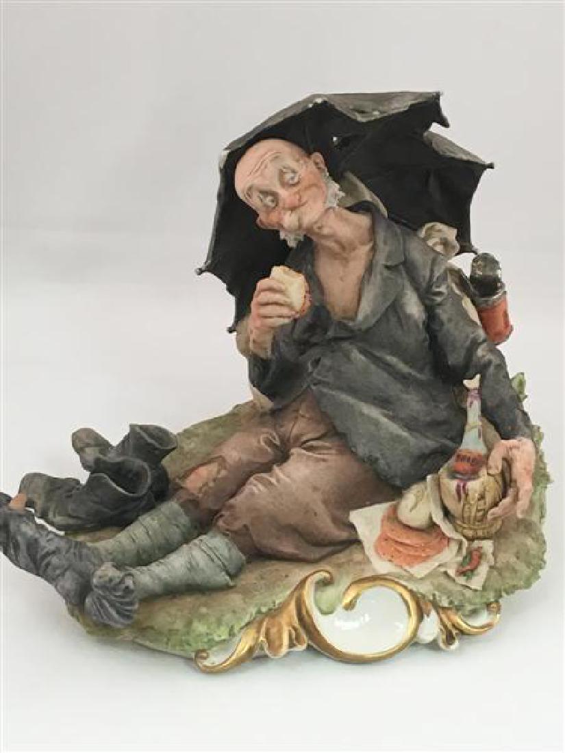 CAPODIMONTE PORCELAIN FIGURE BY G. CALLE: CAPODIMONTE PORCELAIN BY G. CALLE: Figure of an elderly male hobo reclining under an umbrellas while eating a sandwich and drinking wine. Measures: 8" x 6.5" x 7" tall. Condition: minor losses to two