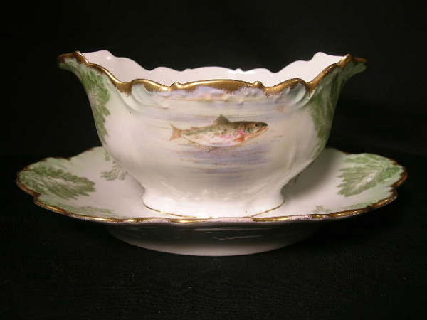 PORCELAIN GRAVY SAUCE BOAT LIMOGES FISH PATTERN: PORCELAIN GRAVY SAUCE BOAT LIMOGES FISH PATTERN - Green and white with gilt trim. Leaf and fish design. Measures 4 1/4" high x 9" wide x 6" deep. No chips, cracks or crazing.