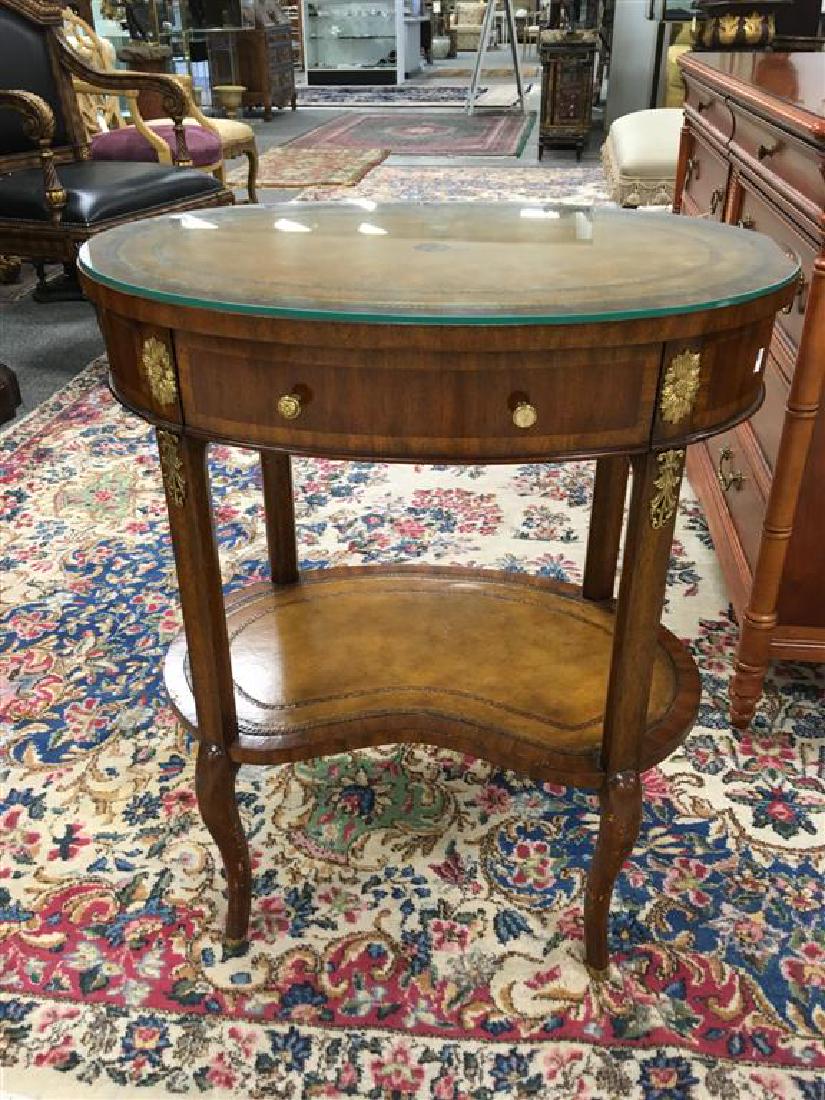 MAITLAND SMITH OVAL LEATHER TOP TABLE: A Maitland-Smith occasional table. Oval shape, embossed leather top, one drawer, one lower kidney-shaped shelf with embossed leather. 25.5" W x 18" D x 30.5" T. Condition: Damage to finish on legs. St