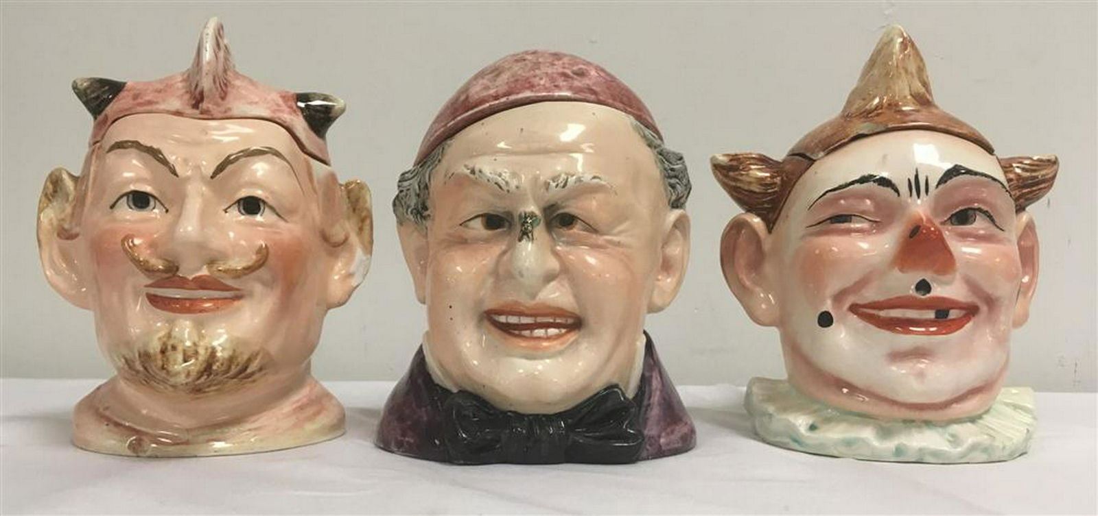 THREE VINTAGE FIGURAL HEAD TOBACCO JARS: BLOCH ETC: Lot of three vintage figural ceramic head form tobacco jars / humidors. Includes a cross eyed man with a fly on his nose, satan, and a clown. The cross eyed man is made by Bernard Bloch. Tallest is th