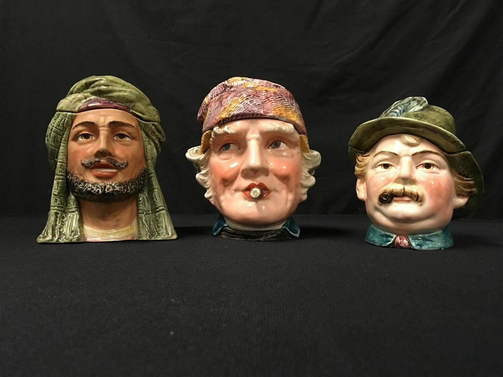 THREE ANTIQUE FIGURAL TOBACCO JAR HEADS: Lot of three antique figural tobacco jars or humidors in the form of heads. Largest is the man with cigar at 7" tall. Condition: tiny flake to base of Arab man, small chip to lid on man with cigar, no