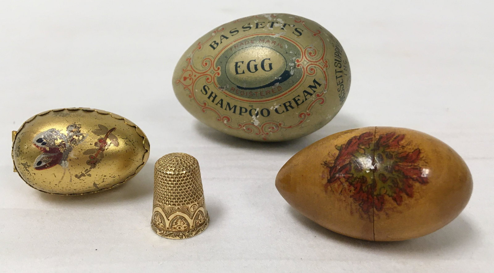 14K GOLD THIMBLE & ANTIQUE EGG LOT: ADVERTISING ET: Sewing / advertisement Lot including a Victorian 14k gold thimble in a small painted egg-shaped box, an egg-shaped soap container for Bassett's Shampoo Cream, and a small turned wood egg-shaped box. C