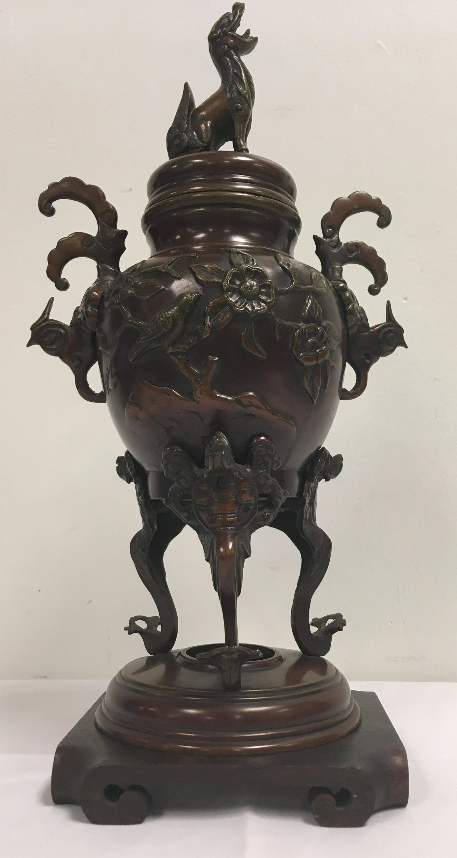ANTIQUE JAPANESE MEIJI BRONZE URN or CENSER: Antique Japanese Meiji period bronze tripod urn or censer. Beautiful deigns in relief. Unmarked, unsigned. Includes wooden stand. Pierced lid to release smoke. Condition: urn sits a tiny bit crooked- 
