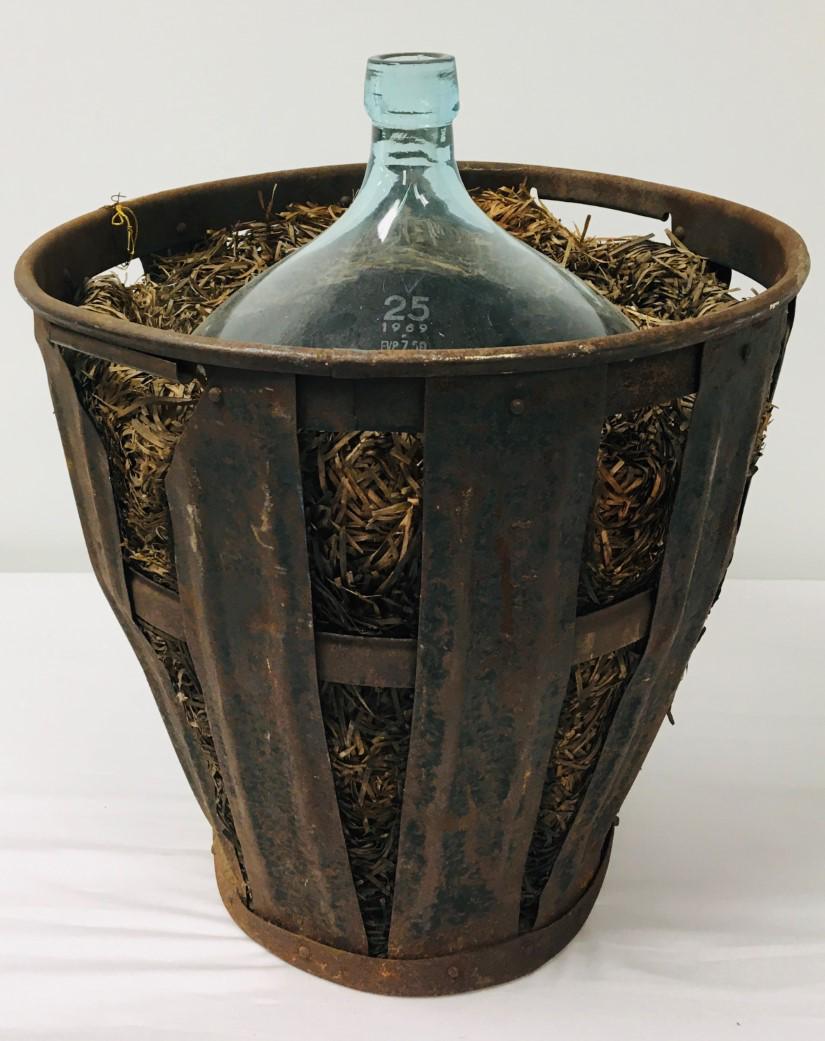 VINTAGE FRENCH IRON & GLASS INSULATED DEMIJOHN: Vintage French iron and glass insulated demijohn bottle with a green tint. Held with straw in an iron basket. Whole assembly measures 21" tall x 17.25" wide. Weight: 19 lbs.