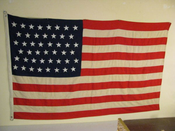 APPROX 100 YEAR OLD AMERICAN FLAG WITH 46 STARS: American flag with forty-six stars. Made from wool fabric. The white strips have yellowed with age. Aluminum grommets. Flag measures 5 feet by 8 feet. Edges of flag are not frayed, some rust marks. Co