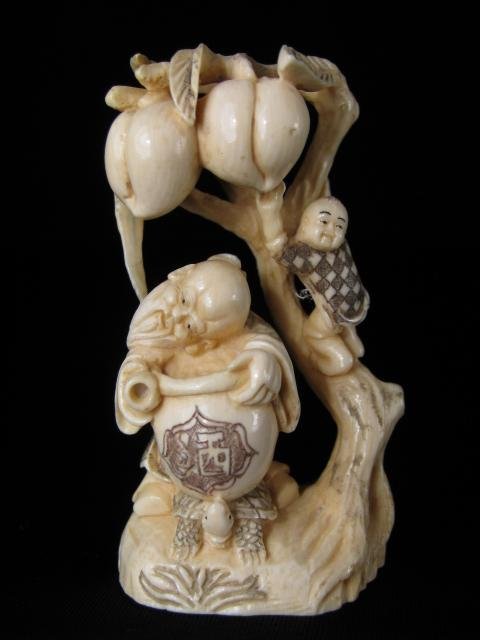 JAPANESE IVORY NETSUKE: 2 FIGURES & PEACH TREE: A carved and polychrome engraved ivory netsuke depicting a old man with a kettle that is set on top of a turtle and a boy climbing a peach tree laden with two large peaches. Signed on the base. Measur