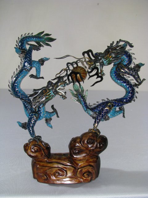 CHINESE SILVER CHAMPLEVE ENAMEL FIGHTING DRAGONS: Two dragons fighting over a flaming pearl done in silver with champleve enameling and set on a carved wood base. Measures 9" tall x 8 1/2" wide. Box measures 11" square x 5" tall. Boxed, weighs 4 lbs