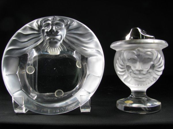 LALIQUE CRYSTAL CIGAR ASH TRAY & LIGHTER TETE DE L: Both items signed Lalique. Table lighter measures 5" tall x 3 1/2" wide with ash tray at 1 1/2" tall x 6" wide. Slight scratches on base. Total weight is 3 lbs 4 oz.