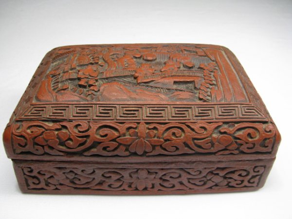CHINESE CARVED CINNABAR LACQUER BOX: Late 19th early 20th century Chinese carved cinnabar box with black lacquer interior. Top of lid has a carved scene with people on a bridge. There is a brass plaque with Chinese character marks on the