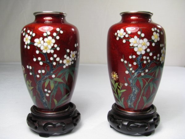 PAIR JAPANESE PIGEON BLOOD CLOISONNE SILVER VASES: Pair of 20th century Japanese pigeon blood cloisonne silver wire vases with carved wood stands. Front of vases have a floral design. Vases measure 4 3/4" tall by 2 1/2" wide, condition is good. Stands