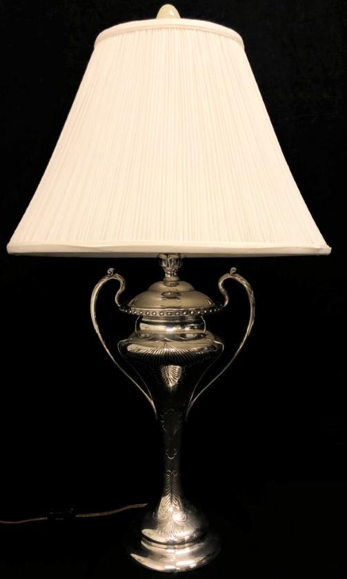 VINTAGE TROPHY STYLE SILVER PLATED TABLE LAMP: Vintage silver plated trophy style table lamp with a white pleated shade. Measures a total of 26" tall to tip of finial, shade is 14.75" wide. Condition: working, may need rewiring for safe use, see i