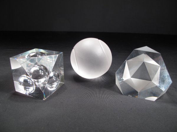 THREE CRYSTAL PAPERWEIGHTS TIFFANY & STEUBEN: Three crystal paperweights. One Steuben semi sphere in a cube. One Steuben Polygon with one translucent side. And one Tiffany Tennis Ball. Semi sphere and Polygon have some surface scratches. Polygon