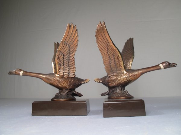 A PAIR OF BRONZE TONE METAL FLYING GEESE BOOKENDS: A pair of mid century flying geese bookends with bronze finish over white metal with cold painted highlights on the tails. Each set to a rectangular metal base and measuring 8" x 7 1/2". Unsigned. Wei