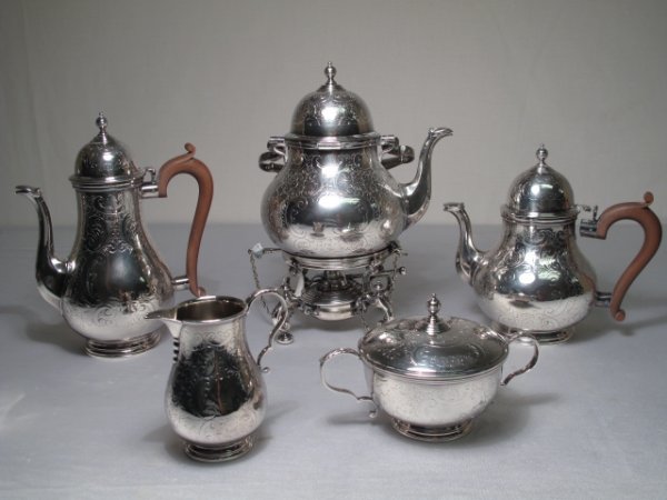 ENGLISH SILVER PLATE FIVE PIECE TEA SET c1940: English silver plated on copper four piece tea set comprising tea pot, coffee pot, hot water pot, creamer and covered sugar bowl. Tea pot has intricate burner and stand with bun feet and chains. Heigh
