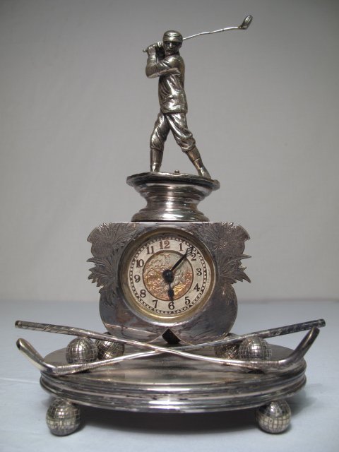 RARE ENGLISH SILVER PLATE GOLF NOVELTY CLOCK: Rare and unusual silver plate clock by The British United Clock co. Golf motif includes large figure of a golfer in mid-swing at the top, a floral engraved clock case on ball feet with two golf clubs 