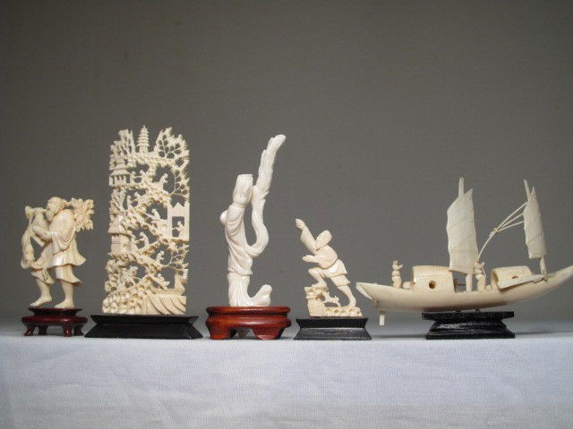 GROUP LOT IVORY CARVED FIGURINES CORAL ETC: Group lot of ivory carved figurines and displays. Includes ornately carved Asian town scene, junk, man carrying fish and scroll, and a man with a dog. Also included is a carved coral figurine (has pie