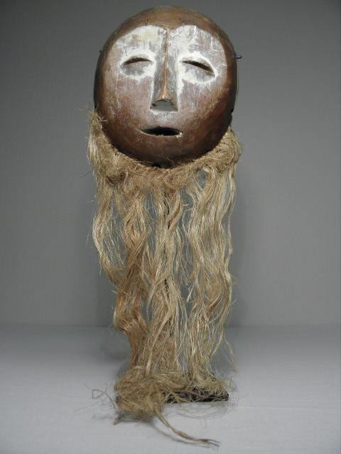 AFRICAN CARVED WOOD TRIBAL MASK: African carved wood tribal mask. White highlights and straw additions on lower portion. Set upon a black metal stand with square flat base. Condition: wear from age, crack to wood on right side, paint